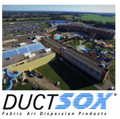 Aerial View Industrial Building With Ductsox Logo | Air Control Products Aerial view of an industrial complex with multiple large buildings and adjacent parking lots surrounded by greenery. The foreground features a colorful playground area and a blue spiral slide. The image includes the DuctSox logo at the bottom, with the text 'Fabric Air Dispersion Products'.