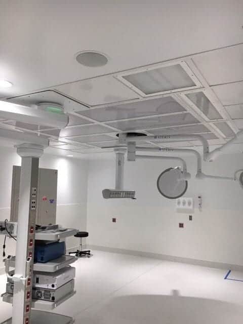 Modern Hospital Operating Room Equipment | Air Control Products A modern hospital operating room featuring advanced equipment. The room has a clean and sterile appearance with white walls and ceiling. Several pieces of equipment, including ceiling-mounted surgical lights and monitors, are visible. There is a movable operating table and various control panels on the walls, indicating a state-of-the-art medical facility.